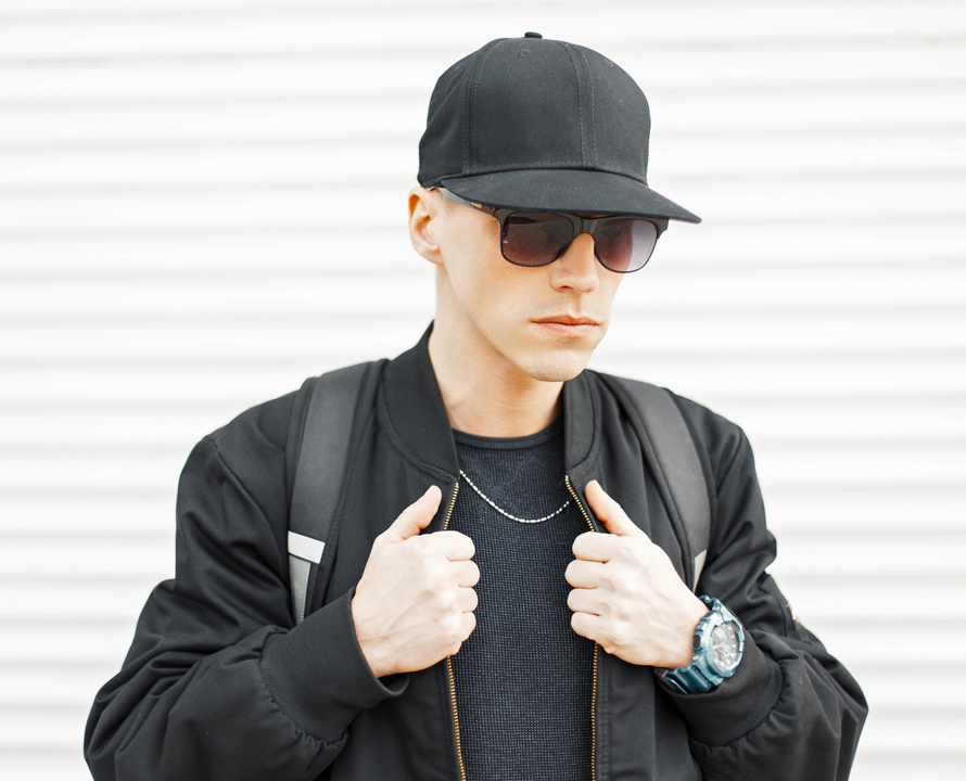 Handsome stylish man in sunglasses and a black baseball cap near a white wall